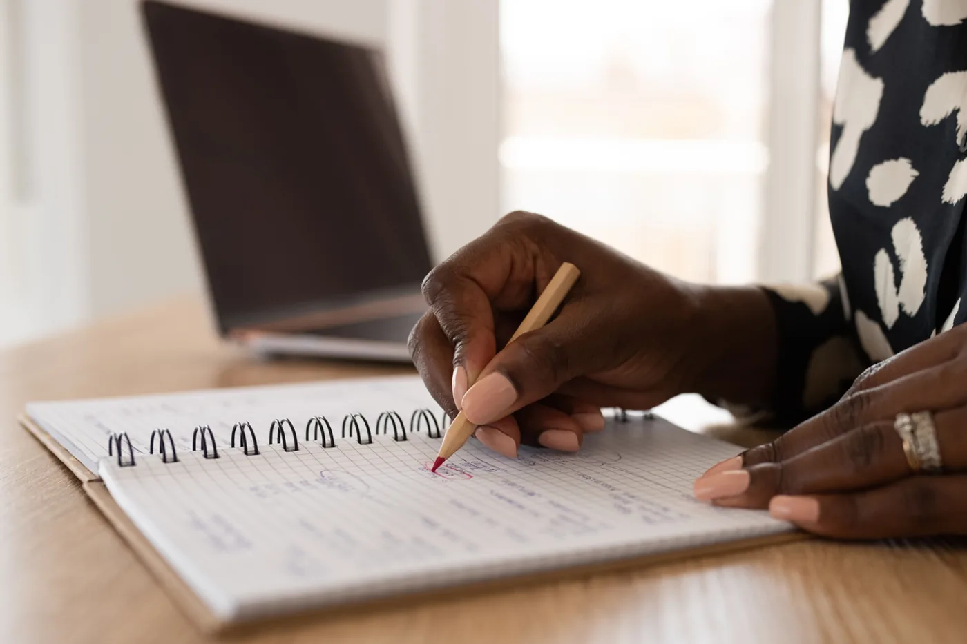 A hand circling a figure on a ruled notepad of mortgage numbers beside a laptop